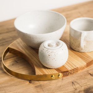 From above stylish minimalistic tea set of light ceramic in dark spots served on oval wooden board