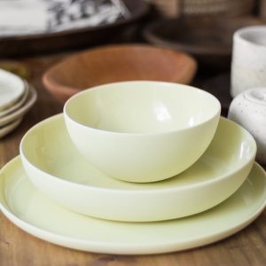 Set of stylish light ceramic crockery including bowls tea cups and plates placed on wooden table